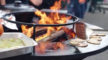 Tütsüde yanan kömür üzerine kızarmış patates ve soğan dilimleri festival pazarında ızgara hazırlama işlemi. Erkekler folyo kutusundan taze sebzeleri bbq ızgarasına koyuyorlar.