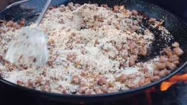 Yanan ateşte büyük metal kazan, piknik partisinde sosisli pilav ve tavuk eti parçaları. Kızarmış yiyecekli barbekü tenceresi, metal kaşıkla pirinçle eti karıştıran adam.