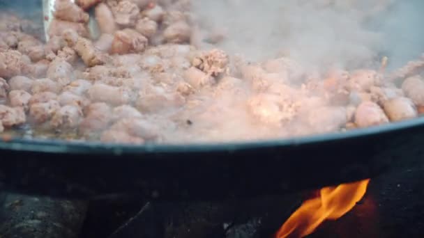 Preparação de comida de rua, linguiças que fritam no grande caldeirão com verduras fritas no fogo ardente. Salsichas cozidas e fumantes em panela de churrasco, conceito de churrasco — Vídeo de Stock