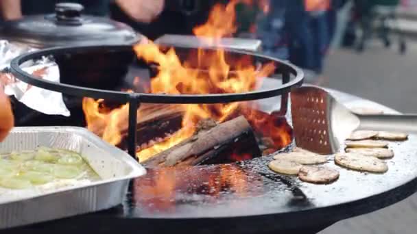 Proces smażenia przyprawionych plasterków ziemniaka i cebuli na węglu drzewnym w palaczu, przygotowanie grilla na targu festiwalowym. Mężczyźni nakładający świeże plastry warzyw na ruszt grilla z pojemnika foliowego — Wideo stockowe