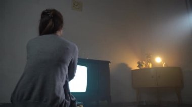 Eski odada loş ışıklandırmalı ve yanıp sönen TV ekranı seyreden bir kadın daha iyi bir kablo TV sinyali bekliyor. Bozuk televizyon, yanıp sönen ekran, karanlık.