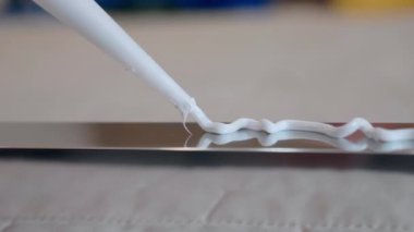 Close up shot of white glue applying in zig zag on metal profile surface, process of bonding material surfaces between them with industrial instruments. Adhesive glue or sealant for fixing, repairing
