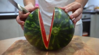 Man cutting ripe watermelon with knife on two halves, juicy red watermelon ready for eating or refreshing smoothie. Sweet fruits cut on pieces in the kitchen, healthy eating concept. High quality 4k