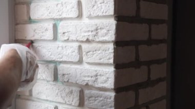 Repairing works on construction site, workman using construction syringe for filling joints between white plates with grout, working on decorative stones on the interior wall. High quality 4k footage