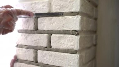 Workman grouting joints between stone tiles with metal grout spatula, builder renovating interior wall with white decorative stones. Process of lining seams on construction site. High quality 4k