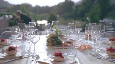 Exit ceremony preparation, crystal glasses decorating round tables, shining and reflecting in sunset. Charming table setting details, trendy composition on banquet party. High quality 4k footage