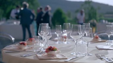 Lüks restoranda çıkış töreni, kristal kadehler parlıyor ve gün batımında güzel dekore edilmiş masaya yansıyor. Tören dekorasyonunun bir parçası olarak içki bardakları, çatal bıçaklar ve çiçek buketleri.