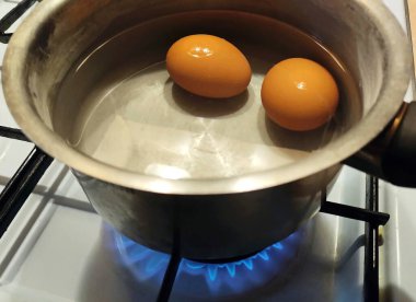 İki tavuk yumurtası kaynar suda bir tencerede kaynatılır. Gaz ocağında portakal yumurtası. Yemek hazırlama. Yumurtaların yakın plan fotoğrafı. Lezzetli ve sağlıklı yemekler.