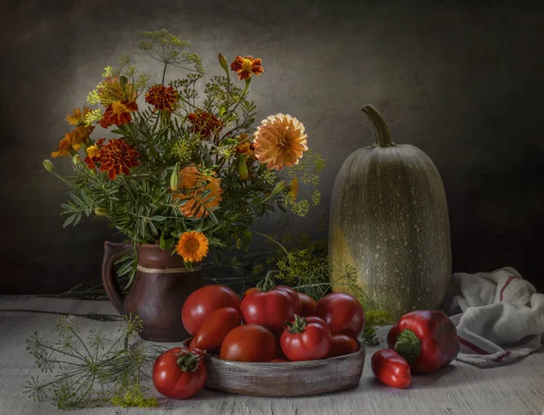 Bir sürahide çiçekler, domatesler ve tahta bir masada balkabağı.