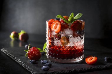 Soğuk, ev yapımı, cam bardakta buzlu çilekli limonata, koyu arkaplanda nane yaprakları ve meyveler..
