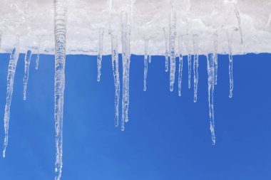Mavi gökyüzüne karşı şeffaf buz saçakları. Kışın güneşte parlayan berrak buz. Donmuş su. Buz saçakları, su damlaları..