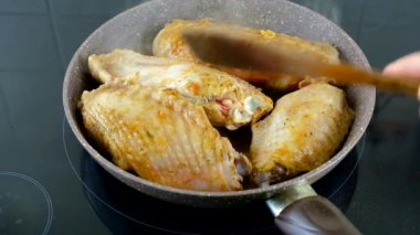 Hindi kanatları siyah elektrikli sobada tavada kızartılıyor. Tahta bir spatulayla bir el kanatlarını çevirir..