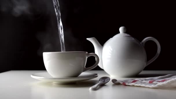 El agua caliente se vierte en una taza de té sobre una mesa blanca. — Vídeo de stock