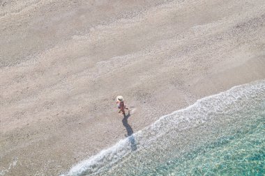 Şapkalı genç atletik kadın, deniz kıyısında kumsalda yalınayak yürüyen mayo. Yaz. Yukarıdan bak. Üst görünüm, copte