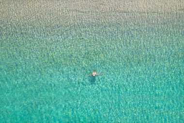 Mayolu ve şapkalı genç bir kadın sahile yakın deniz dalgalarında yüzüyor. Yukarıdan bak. Üst, drone görünümü