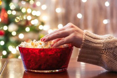 Evde yalnız bir kadın Noel ağacının yanında patlamış mısır yiyor..