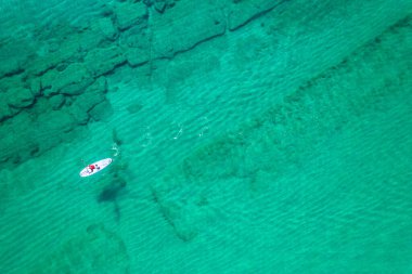 Aquamarine 'de SUP' de kürek çeken yalnız bir adam, lagündeki mercanlı mavi deniz suyu. Havadan görüntülü raket. Sörf