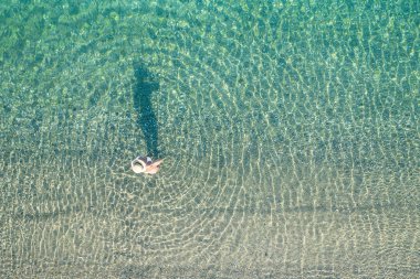 Mayolu ve şapkalı genç atletik kadın kumsalda denizde duruyor. Yaz. Yukarıdan bak. Üst manzara, helikopter.
