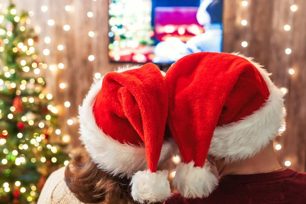 クリスマス カップル男と女で赤いサンタクロースの帽子テレビを見て — ストック写真