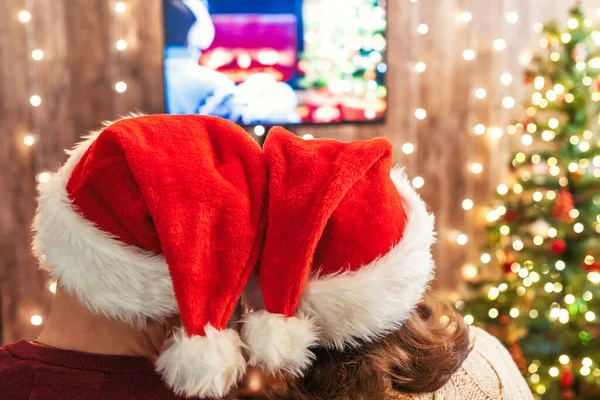 クリスマス カップル男と女で赤いサンタクロースの帽子テレビを見て — ストック写真