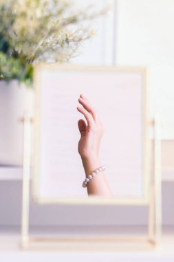 Masadaki aynada yansıyan inci bilezikli kadın makyaj aksesuarlarıyla makyaj masasında. Kişisel bakım. Dikey