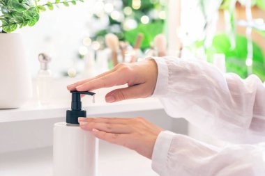 Makyaj malzemeleriyle makyaj masasının yanında oturan bir kadın eline günlük krem sürüyor. Noel ağacının yansıması, masa aynasında ampuller..