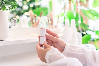 Makyaj aksesuarları ve masa aynasıyla makyaj masasının yanında oturan bir kadın. Beyaz iç mekan