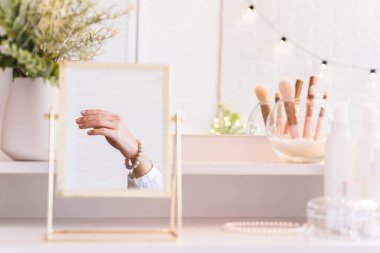 Masadaki aynada yansıyan inci bilezikli kadın makyaj aksesuarlarıyla makyaj masasında. Kişisel bakım. Beyaz iç mekan