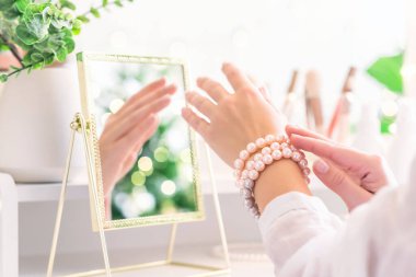 Kadın, makyaj malzemeleriyle birlikte sehpanın yanında duran inci bilezikleri veriyor. Noel ağacının yansıması, masa aynasında ampuller..