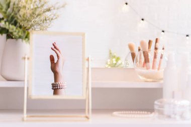 Noel, ampuller, okaliptüs, köknar makyaj malzemeleriyle makyaj masasındaki vazoda çam dalları. İnci bilezikler takmış bir kadının masa aynasında yansıması.