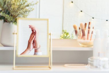 Masadaki aynada yansıyan inci bilezikli kadın makyaj aksesuarlarıyla makyaj masasında. Kişisel Bakım. 