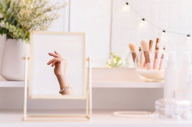 Noel, ampuller, okaliptüs, köknar makyaj malzemeleriyle makyaj masasındaki vazoda çam dalları. İnci bilezikler takmış bir kadının masa aynasında yansıması.