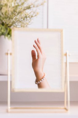 Masadaki aynada yansıyan inci bilezikli kadın makyaj aksesuarlarıyla makyaj masasında. Kişisel bakım. Dikey