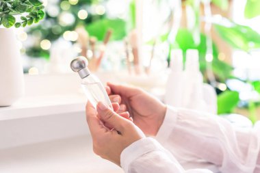 Makyaj aksesuarları ve masa aynasıyla eline parfüm süren bir kadın. Kişisel Bakım. 