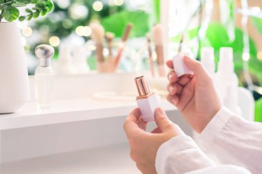 Makyaj aksesuarları ve masa aynasıyla makyaj masasının yanında oturan bir kadın. Beyaz iç mekan