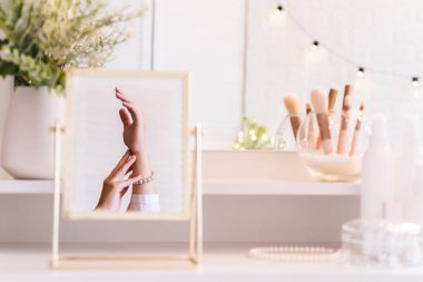 İnci bilezikler takmış bir kadının masa aynasında yansıması. Noel, ampuller, okaliptüs, köknar makyaj malzemeleriyle makyaj masasındaki vazoda çam dalları. Dikey