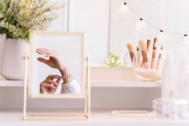 Masadaki aynada yansıyan inci bilezikli kadın makyaj aksesuarlarıyla makyaj masasında. Kişisel bakım. Beyaz iç mekan