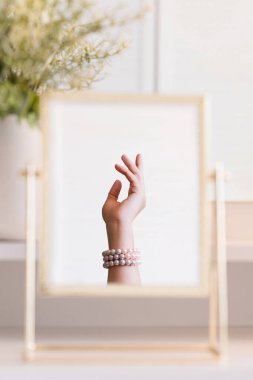 Masadaki aynada yansıyan inci bilezikli kadın makyaj aksesuarlarıyla makyaj masasında. Kişisel bakım. Dikey