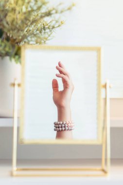 İnci bilezikler takmış bir kadının masa aynasında yansıması. Noel, ampuller, okaliptüs, köknar makyaj malzemeleriyle makyaj masasındaki vazoda çam dalları. Dikey