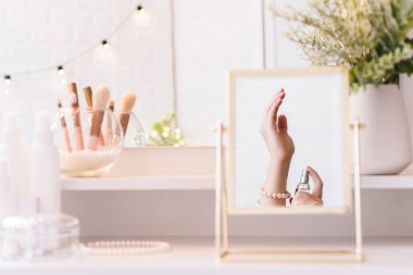 Masa aynasındaki kadın parfümünü eline sürerken yansıması. Kadın parti hazırlığı. Noel, ampuller, okaliptüs, köknar, makyaj malzemeleriyle makyaj masasındaki vazoda çam dalları.. 