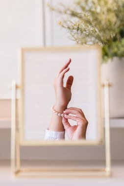 Noel, ampuller, okaliptüs, köknar makyaj malzemeleriyle makyaj masasındaki vazoda çam dalları. İnci bilezikler takmış bir kadının masa aynasında yansıması.