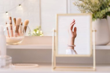 Noel, ampuller, okaliptüs, köknar makyaj malzemeleriyle makyaj masasındaki vazoda çam dalları. İnci bilezikler takmış bir kadının masa aynasında yansıması.