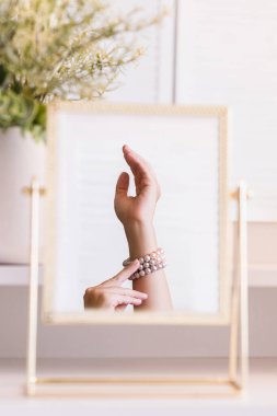 İnci bilezikler takmış bir kadının masa aynasında yansıması. Noel, ampuller, okaliptüs, köknar makyaj malzemeleriyle makyaj masasındaki vazoda çam dalları. Dikey