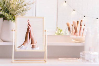 İnci bilezikler takmış bir kadının masa aynasında yansıması. Kadın parti hazırlığı. Noel, ampuller, okaliptüs, köknar, makyaj malzemeleriyle makyaj masasındaki vazoda çam dalları.. 