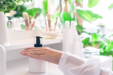 Kadın eline günlük krem sürüyor makyaj malzemeleri ve masa aynasıyla makyaj masasının yanında oturuyor.. 