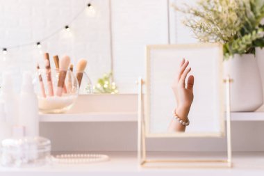 Masadaki aynada yansıyan inci bilezikli kadın makyaj aksesuarlarıyla makyaj masasında. Kişisel Bakım. 