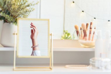 Masadaki aynada yansıyan inci bilezikli kadın makyaj aksesuarlarıyla makyaj masasında. Kişisel Bakım. 