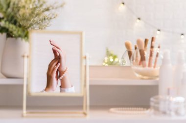 Noel, ampuller, okaliptüs, köknar makyaj malzemeleriyle makyaj masasındaki vazoda çam dalları. İnci bilezikler takmış bir kadının masa aynasında yansıması.