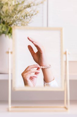 Masadaki aynada yansıyan inci bilezikli kadın makyaj aksesuarlarıyla makyaj masasında. Kişisel bakım. Dikey