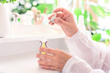 Makyaj aksesuarları ve masa aynasıyla eline parfüm süren bir kadın. Noel, ampuller, okaliptüs, köknar, bir vazoda çam dalları.